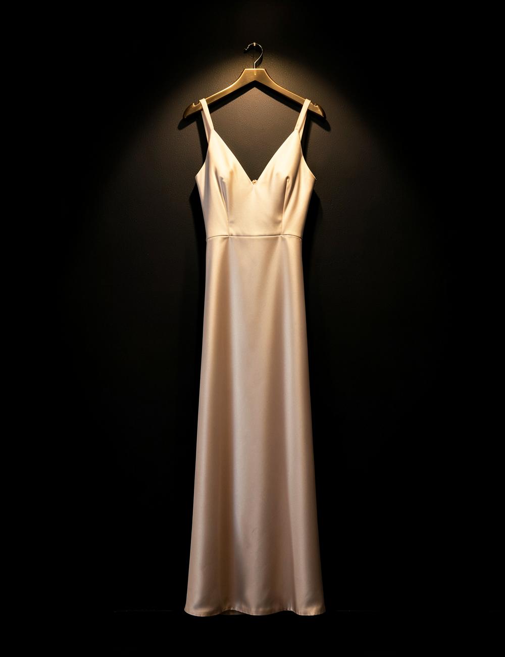Beige satin evening gown on a hanger against a dark wall